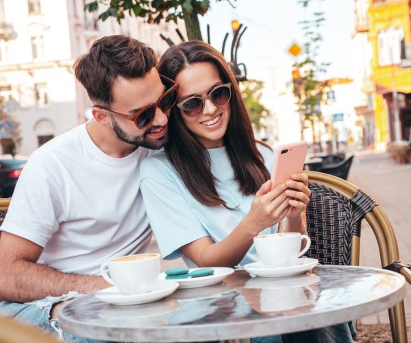 Smiling beautiful woman and her handsome boyfriend. Drinking tea, coffee at veranda cafe outdoors